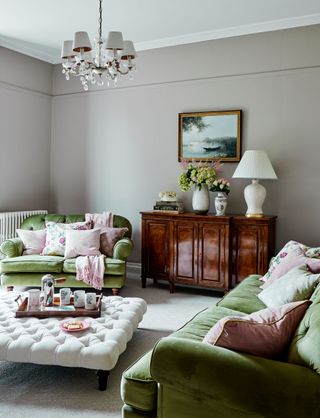 living room with green sofas and pink cushions and buttoned footstool and polished wood sideboard with flowers