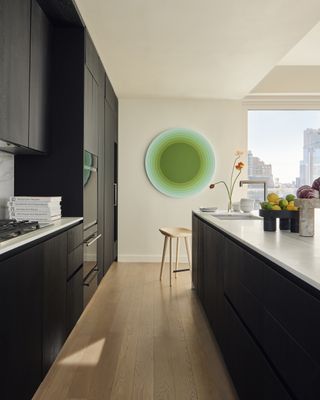 dark kitchen with white worktops and round green artwork on wall