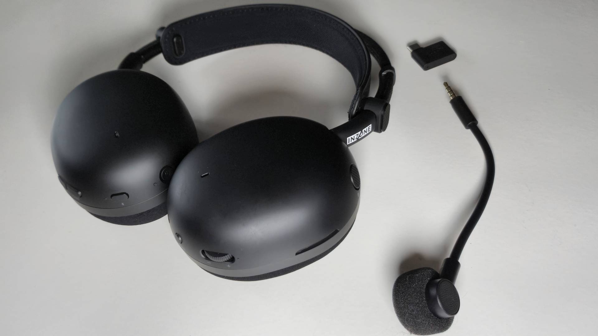 Photo of a black Sony headset sitting on a white table, with its 2.4GHz wireless dongle and microphone to its side.