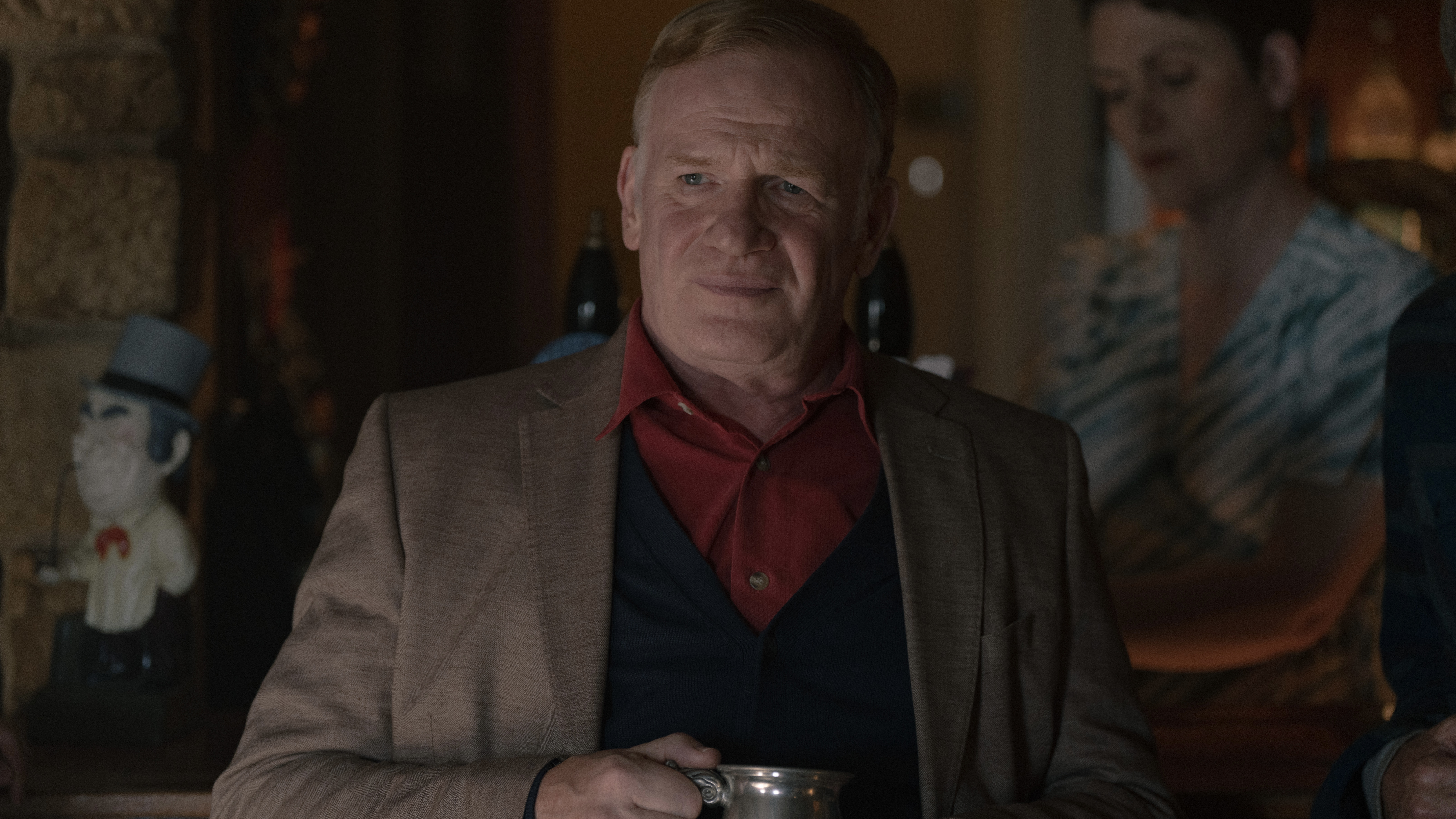 Mark Lewis Jones in a brown jacket and red shirt holds a tankard as Gruffudd Prosser in The Red King.