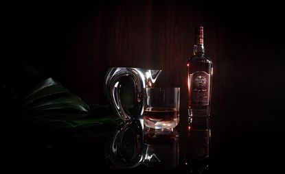 Bottle of rum from rapper Skepta and Havana Club, a glass and silver carafe on a reflective surface against a dark wood background