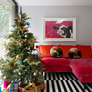 Wrapped presents beneath Christmas tree decorated with colourful baubles next to red sofa in living room