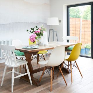 A wooden dining table with mix and match chairs next to a watercolour effect wall