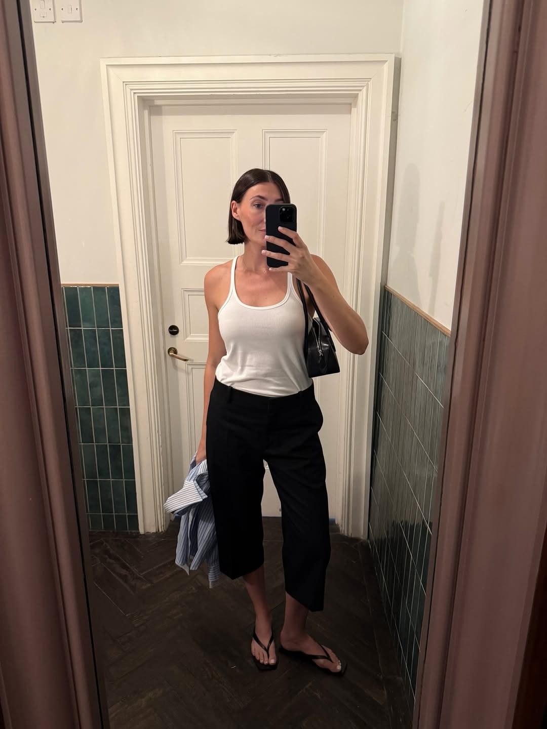 Influencer Sarah wears a white scoop neck tank with a pair of cropped black pants and flip-flops.