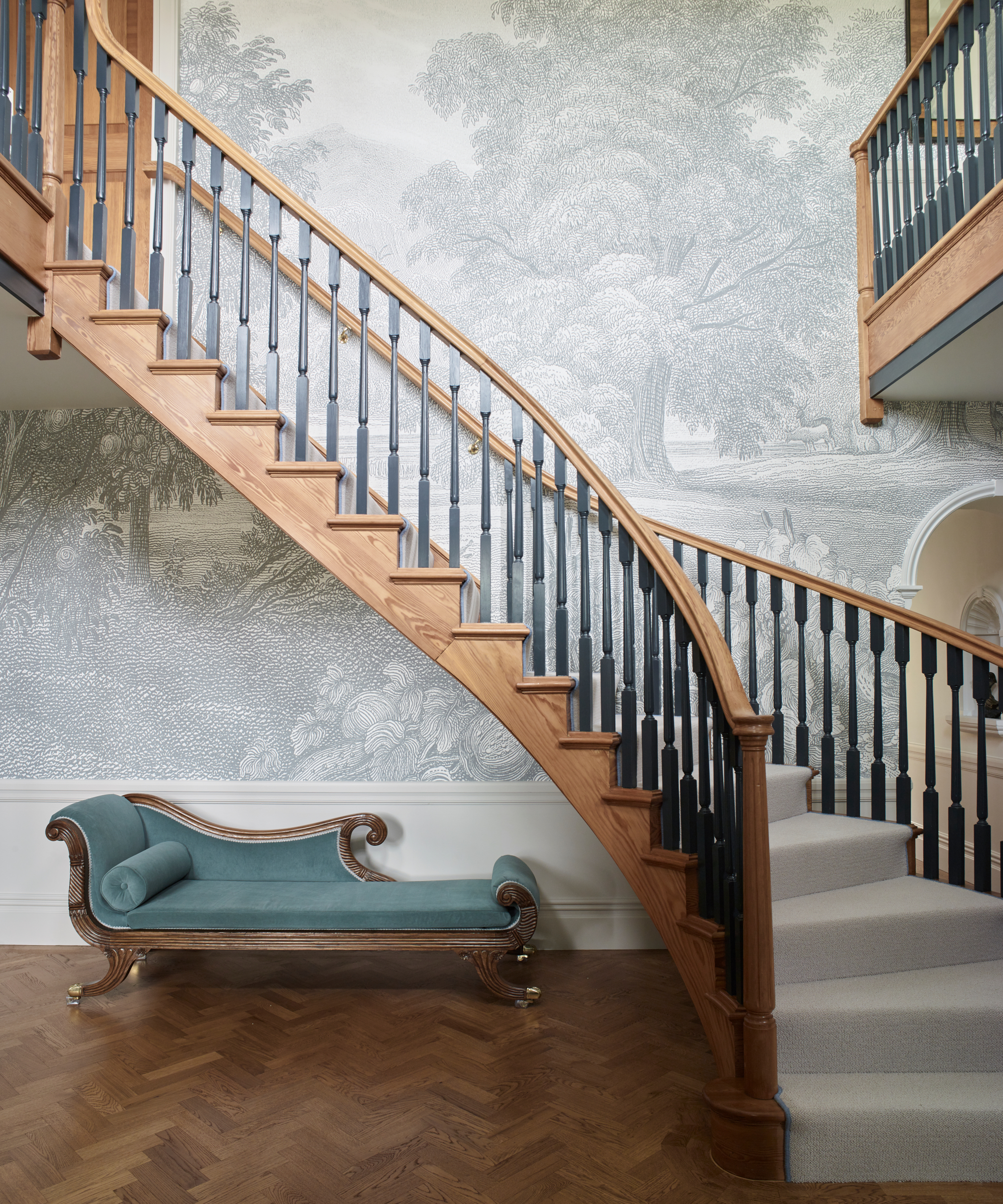 couloir avec escalier en bois, moquette neutre et sol en bois à chevrons, chaise bleu sarcelle et papier peint arbre gris