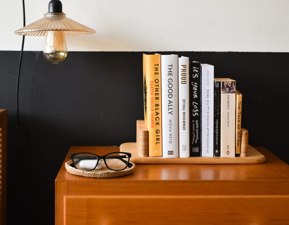 A dresser table with books stacked on a small wooden holder and a pendant lamp hanging from overhead