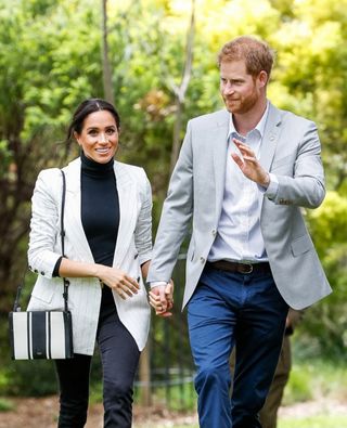 Prince Harry and Meghan Markle walking hand in hand, Harry waving
