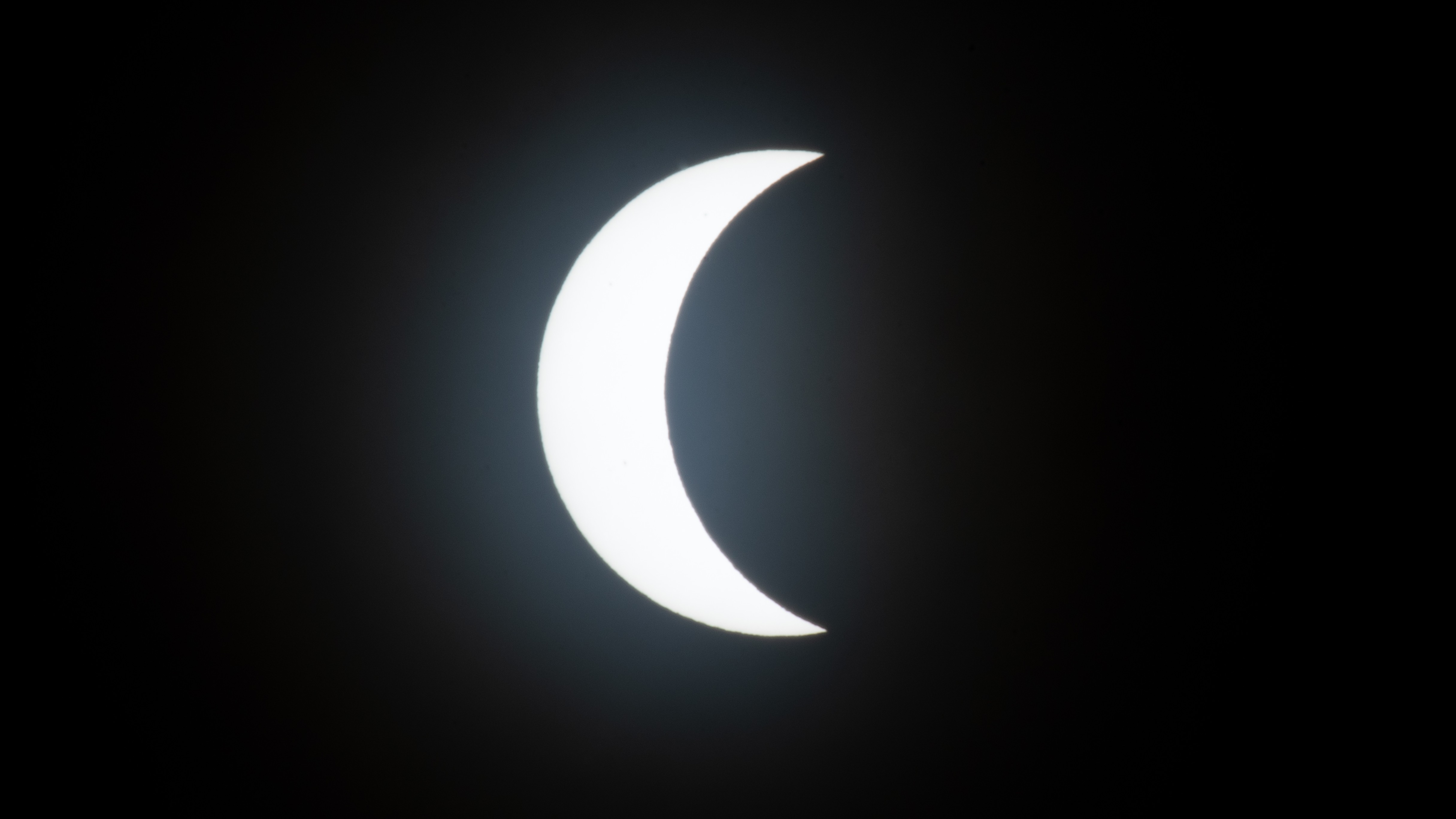 The sun's disk is photographed as a white crescent in a black sky during the partial phase of a total solar eclipse.