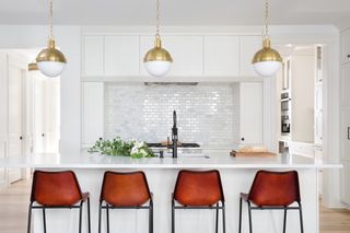 An all white kitchen with island chairs in maroon