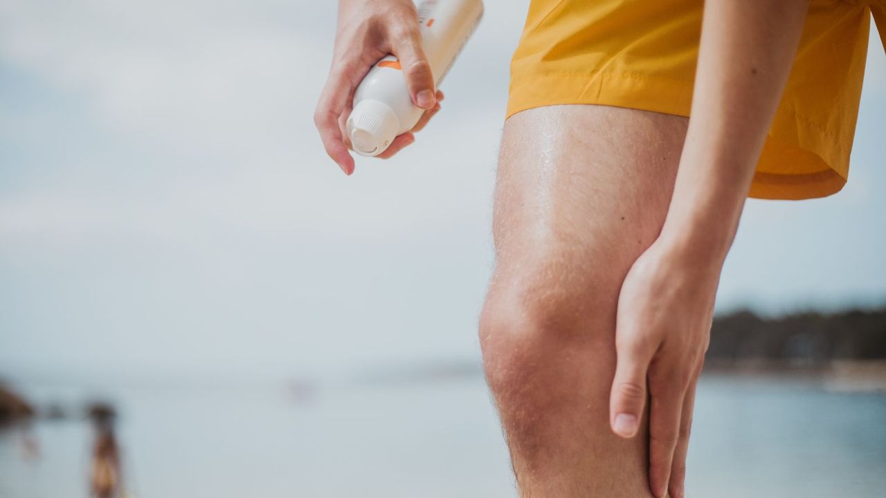 A male spritzes his leg with spray sun screen at beach