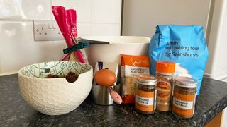 a photograph of christmas pudding ingredients including flour, spices, raisins, egg, almonds, and sugar