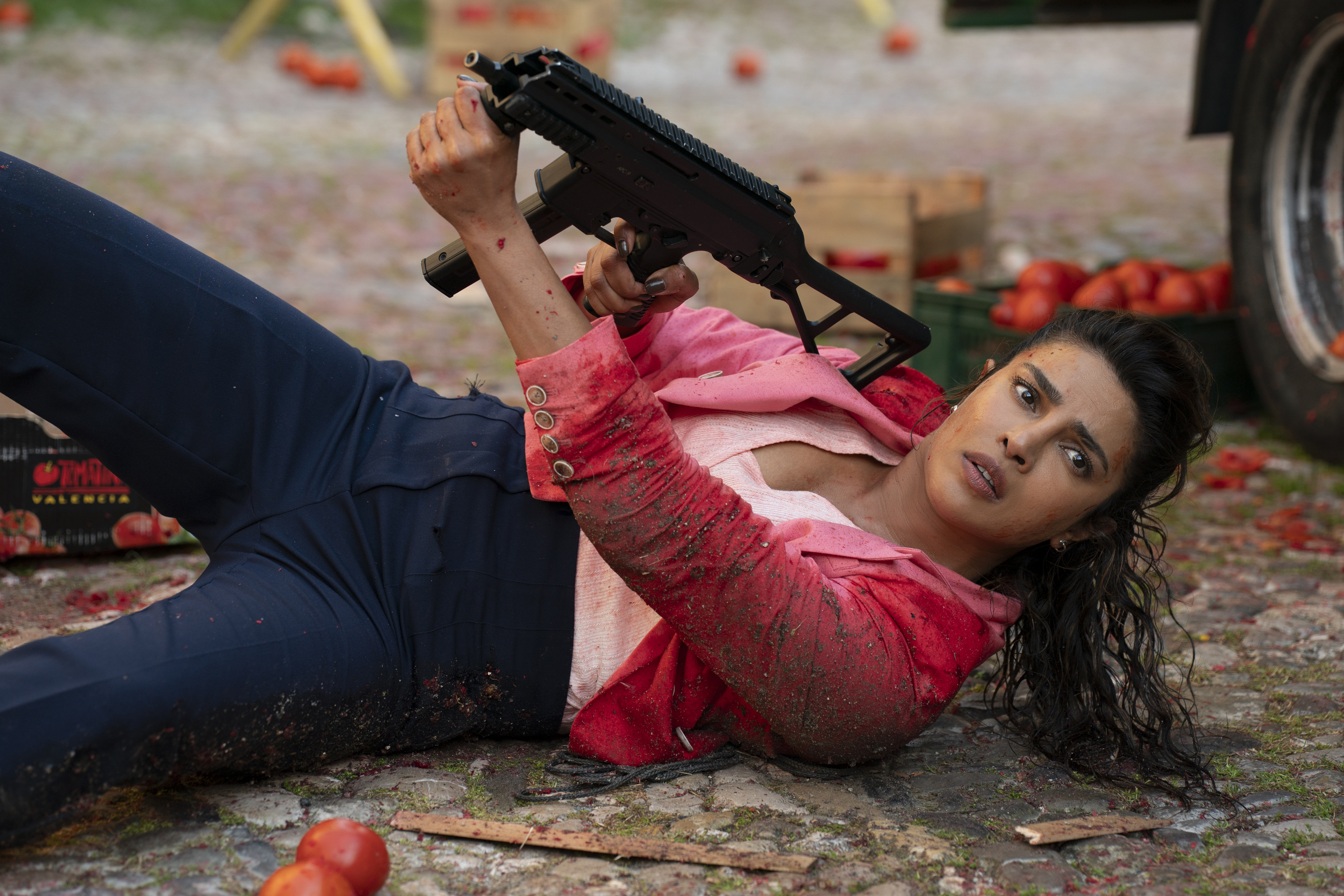 priyanka chopra lying on the ground with a gun amid a fallen tomato cart in the movie heads of state