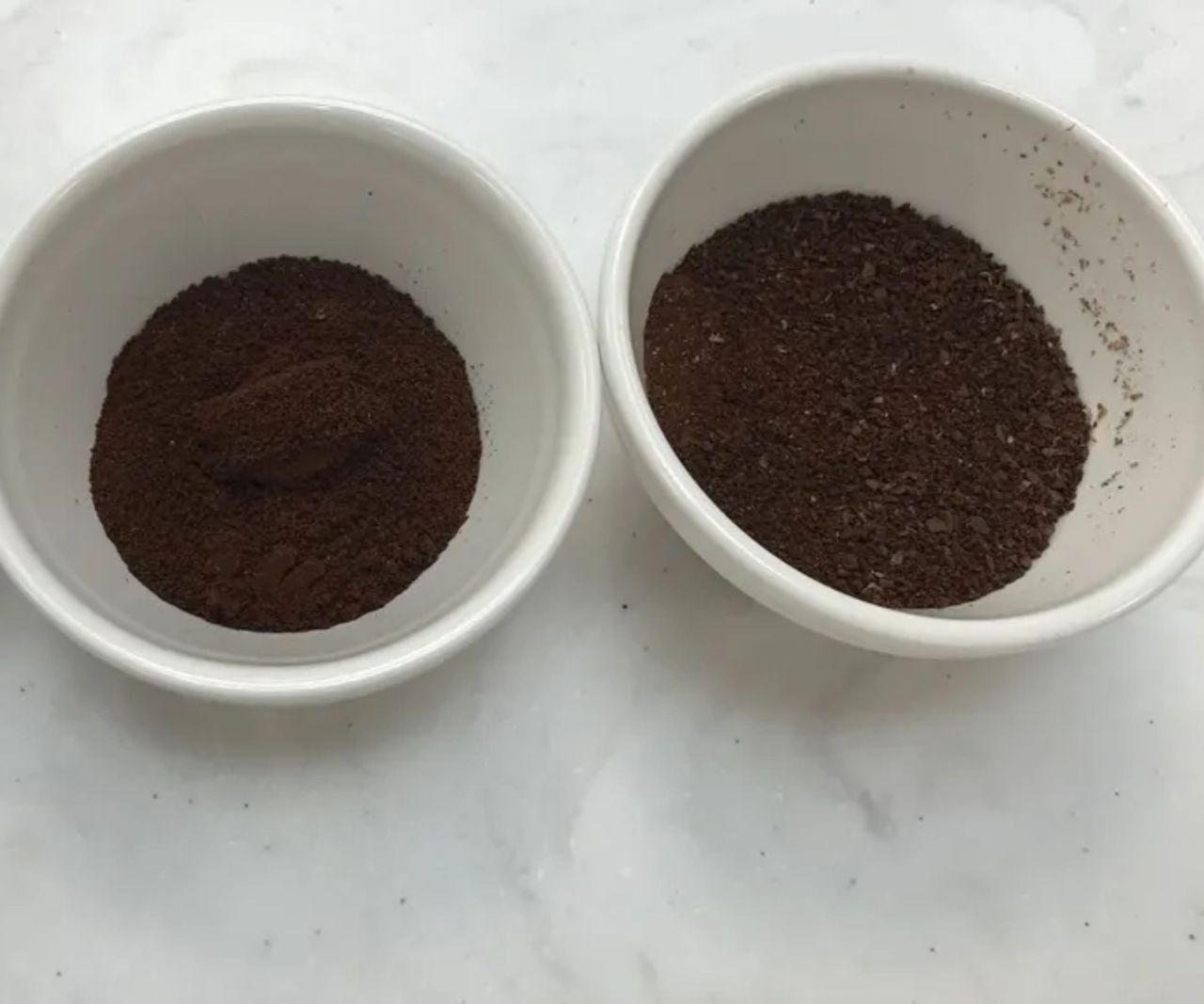 Two white pinch bowls filled with fine and course coffee grounds on a white counter.