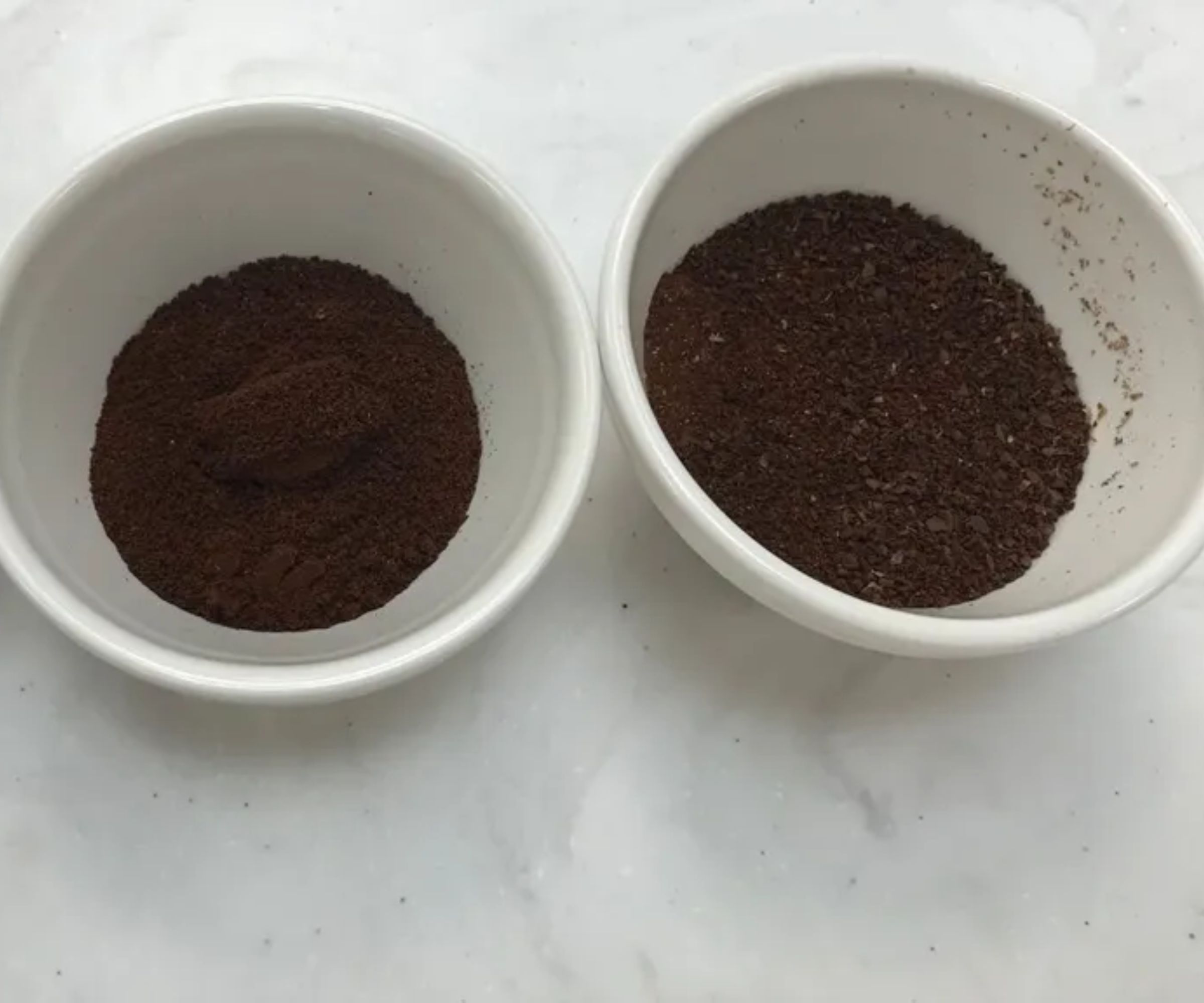 Two white pinch bowls filled with fine and course coffee grounds on a white counter. 
