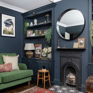 Dark painted living room with shelving and fireplace, round mirror, and table lamp