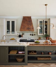 large white and sage green kitchen with parquet flooring, copper cooker hood, green island, white countertops, brass fixtures and fittings, glazed wall units