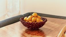 A basketweave bowl on top of table with lots of lemons inside it