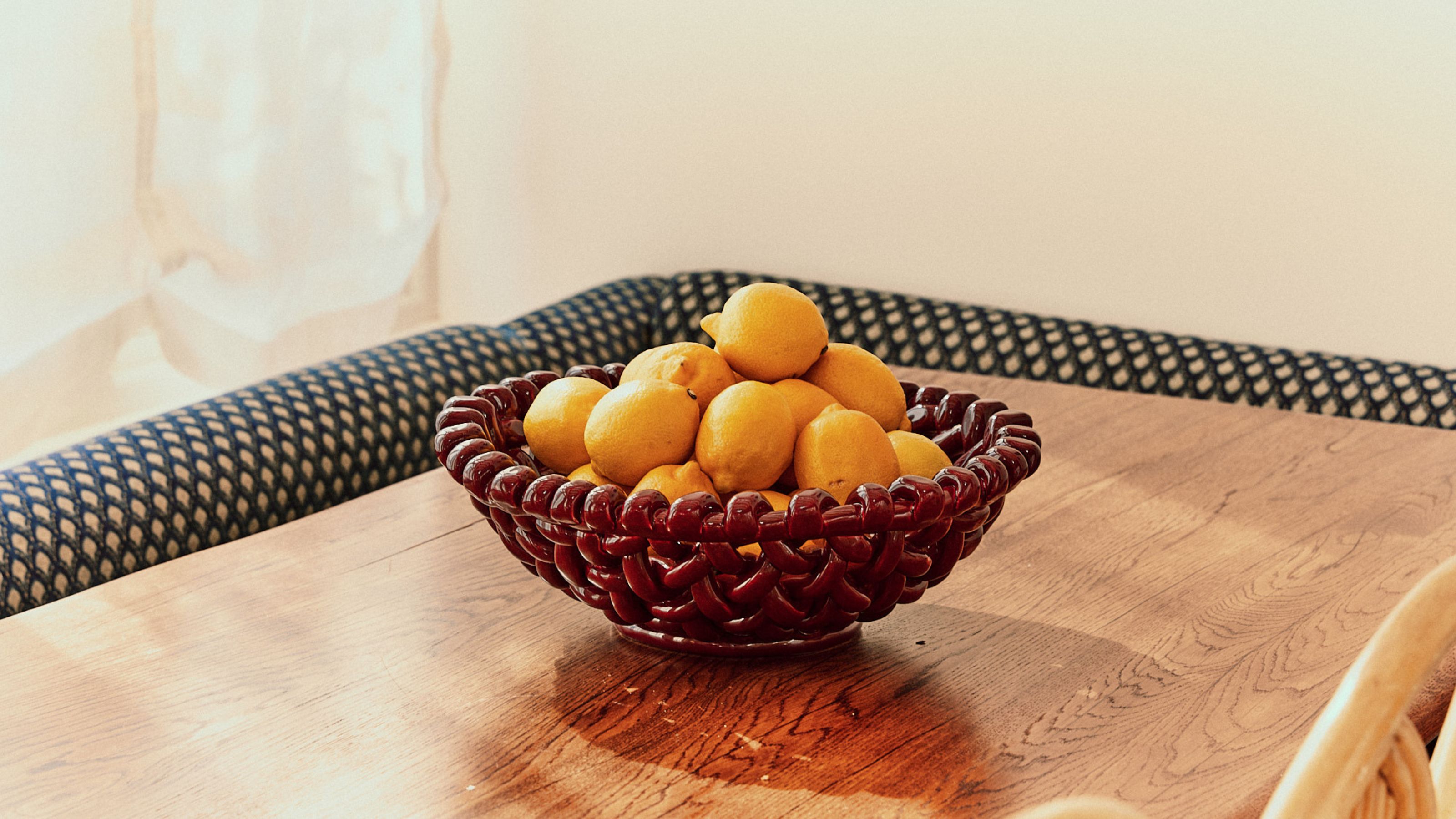 A basketweave bowl on top of table with lots of lemons inside it 