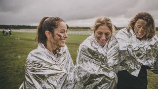 Three women wearing emergency blankets after a race