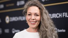 Image of Olivia Colman smiling with grey curly long hair over one shoulder