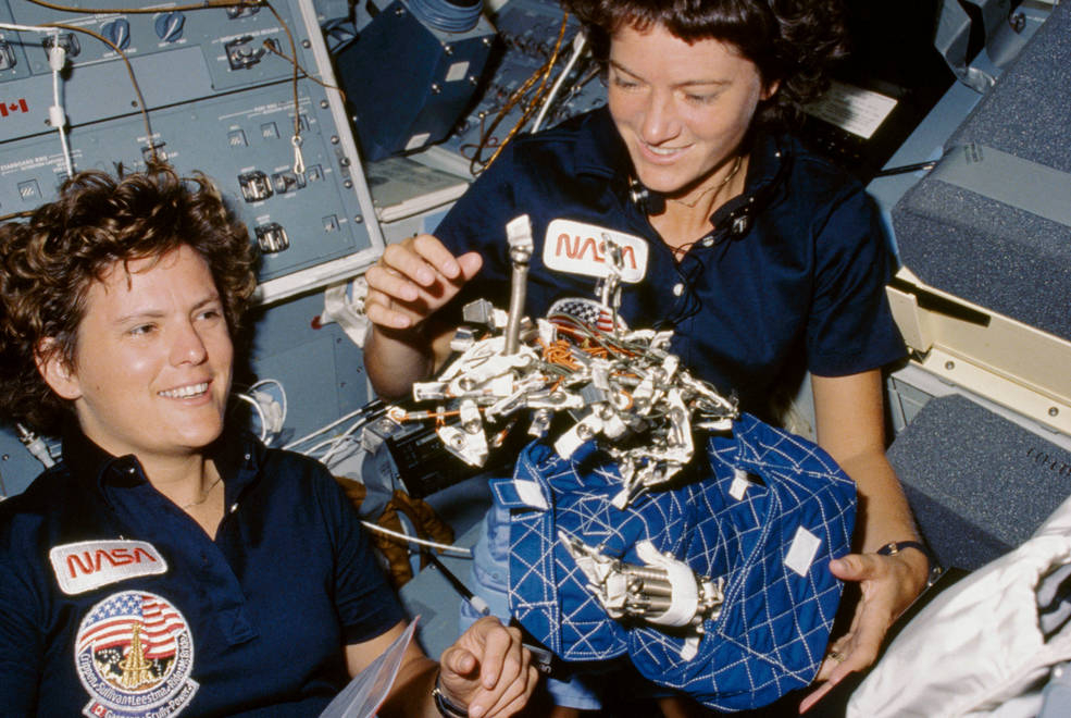 two women float in a space shuttle with a blue apparatus
