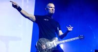 Mark Tremonti throws the horns and points to something during a live performance with Creed. His signature PRS singlecut is strapped on his shoulder.