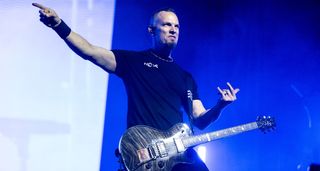 Mark Tremonti throws the horns and points to something during a live performance with Creed. His signature PRS singlecut is strapped on his shoulder.