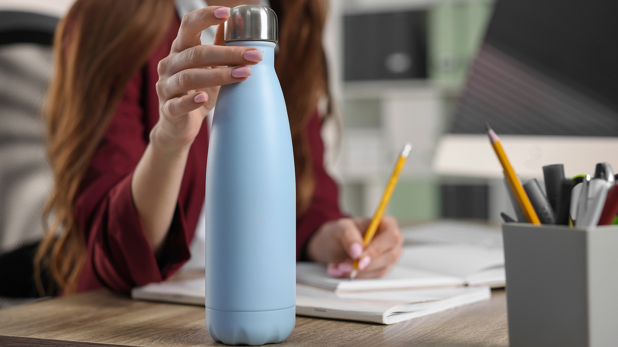 Person holding a reusable water bottle while writing in a book in a home office