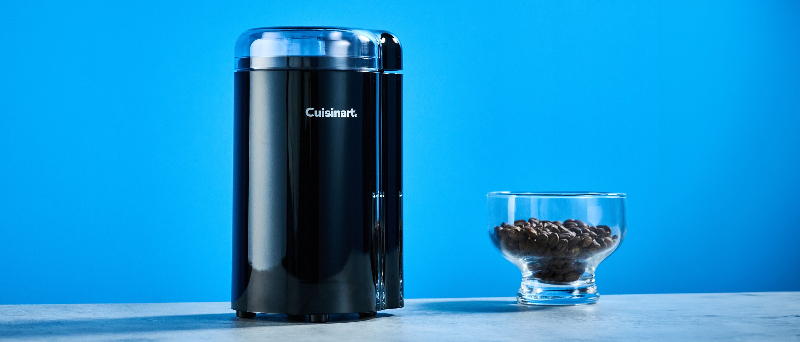 the cuisinart coffee grinder photographed against a blue background showing its blades and canister