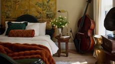 Soulful, eclectically layered bedroom featuring tea and terracotta bedding accents, a patterned decorative folding screen, cello, and antique wood and brass details scattered throughout