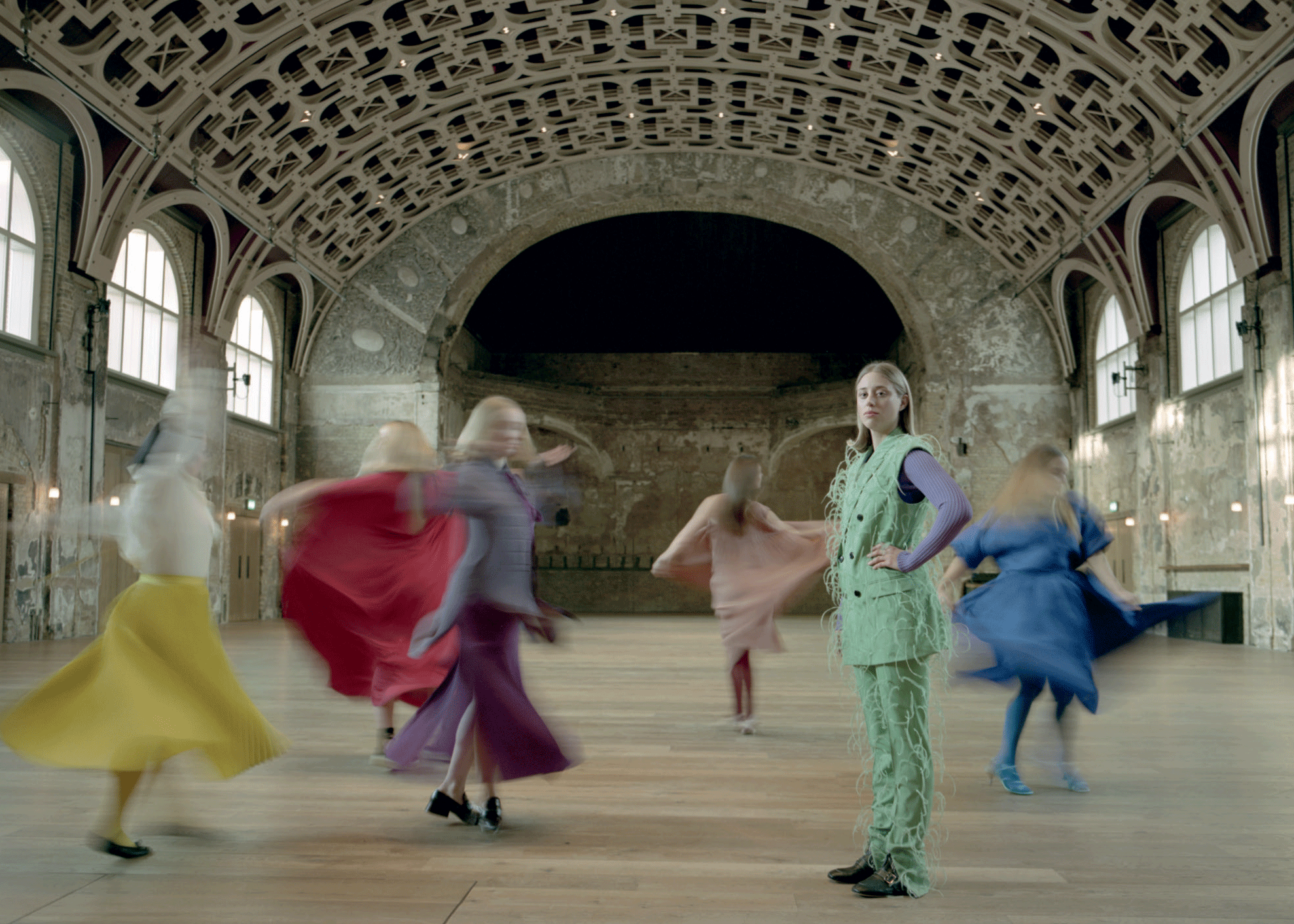 One unmoving woman, dressed in green, surrounded by the blurred images of dancers