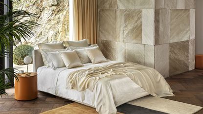 Luxury bedding from Frette on a bed against gold walls.