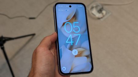 The Google Pixel 9a held in the photographer's hand. The display shows the lock screen, with the time and unlocked symbol visible. 