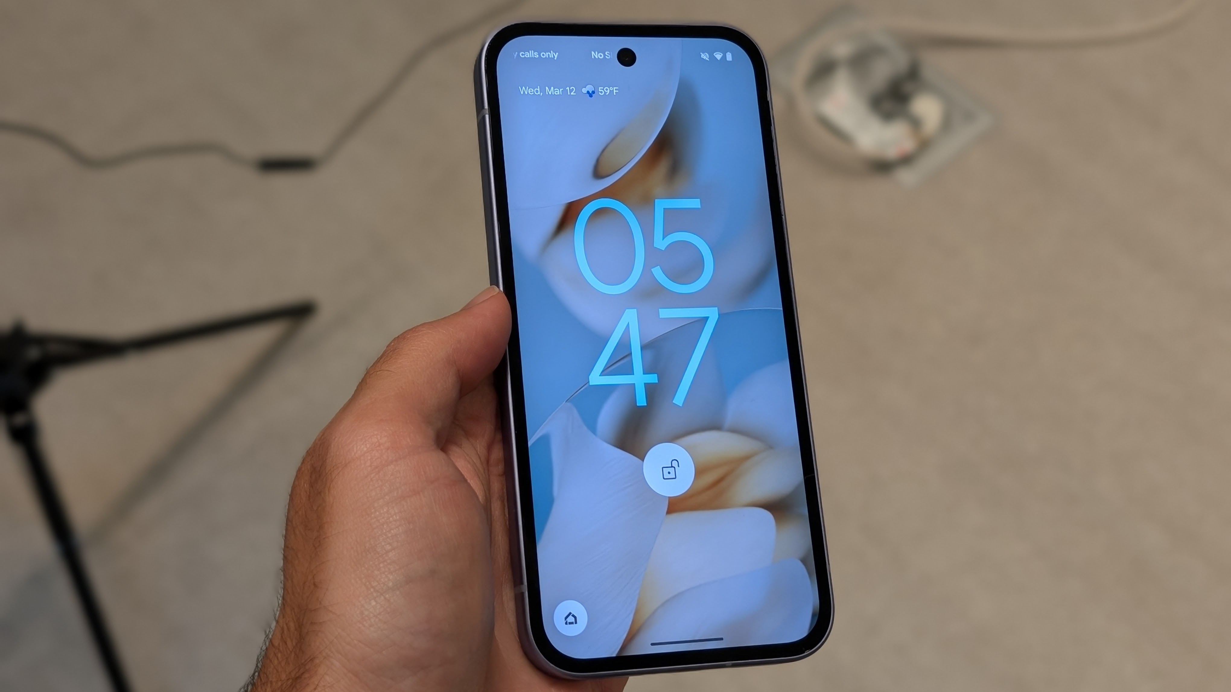 The Google Pixel 9a held in the photographer's hand. The display shows the lock screen, with the time and unlocked symbol visible.