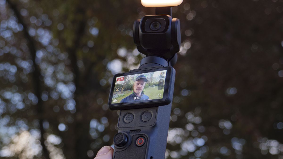 DJI Osmo Pocket 4 vlogging camera with natural background at golden hour, and the user in the frame of the screen