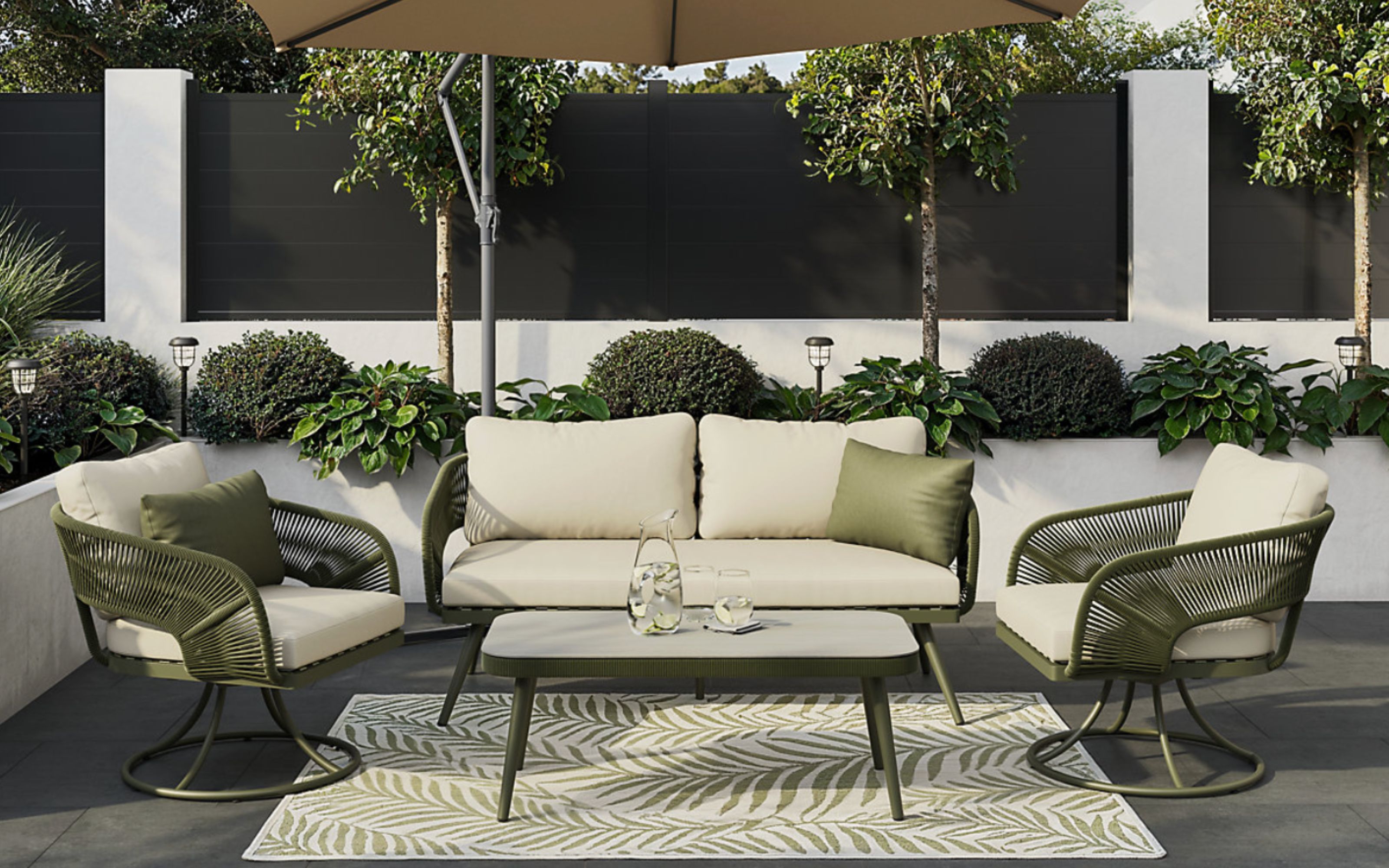 GoodHome Giza Green Metal 4 Seater Coffee Set with green scatter cushions sitting on a dark patio with a green and white rug, underneath a parasol