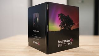 The Printique photo book propped open so you can see the front and rear covers simultaneously; the front image shows an aurora and the words 'TechRadar Photo Book'.
