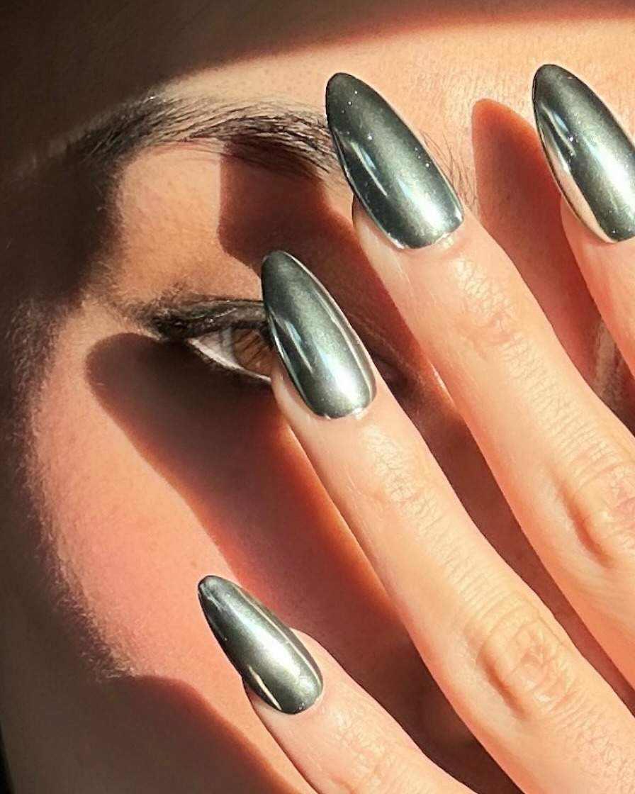 Close-up photo of a person&amp;rsquo;s hand showcasing a silver chrome manicure on almond nails.