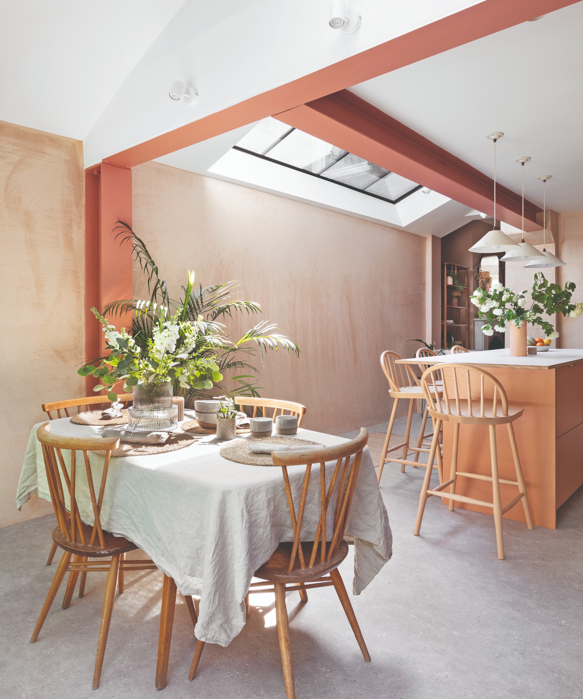 A bright, airy kitchen with a dining area visually separated with beams painted a contrasting terracotta red shade