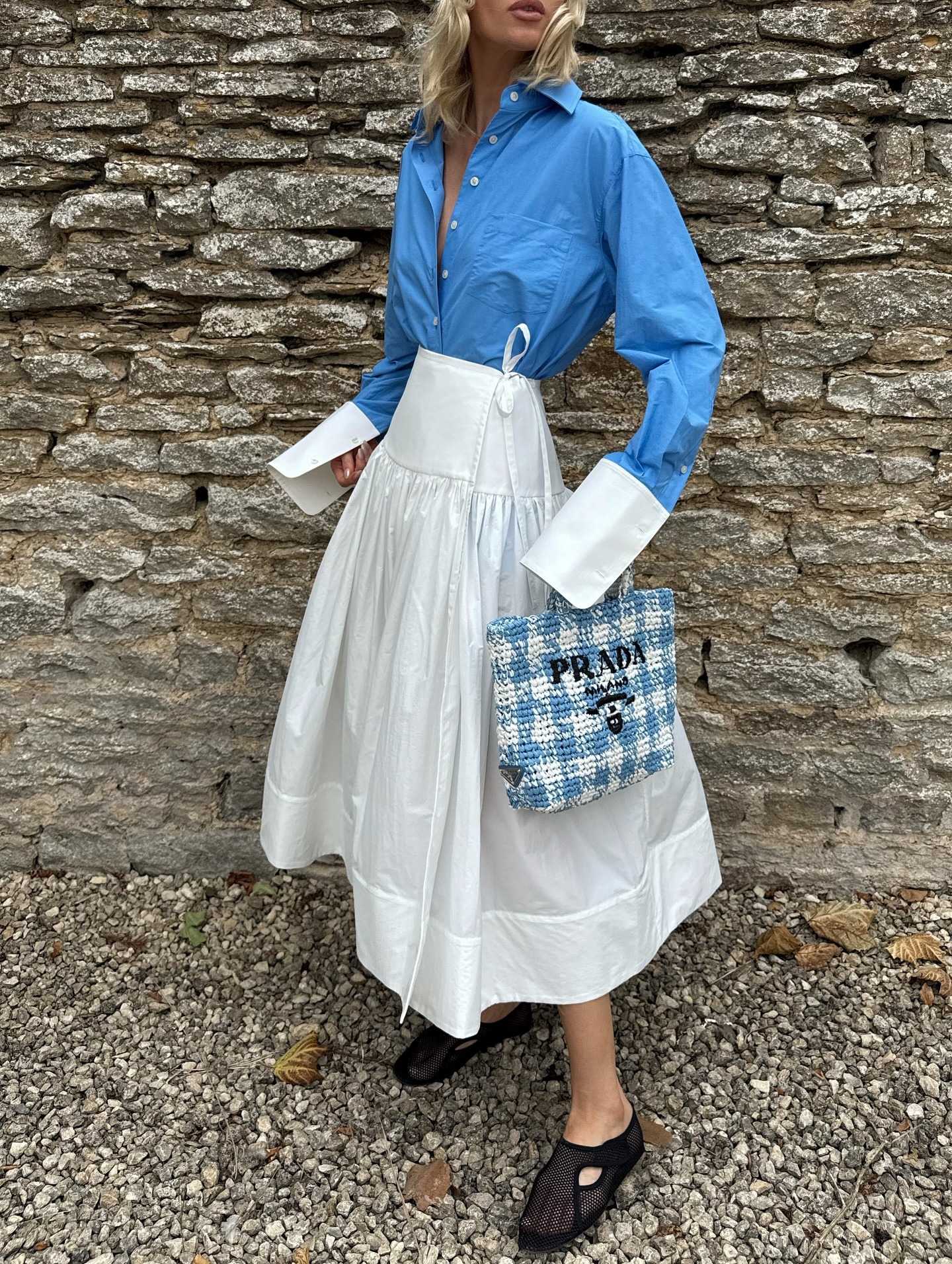 Elsa Hosk wearing a head scarf, Helsa blue button-down shirt and white poplin midi skirt, and Alaia fishnet slippers in the Cotswolds