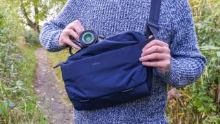 A man reaching for a camera inside the Bellroy Venture 10L Sling Camera Edition bag