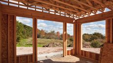 Half constructed wooden home addition looking from the insight out where French doors will be out onto unmanicured or landscaped green space