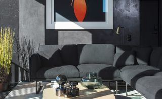 Interior view of At Six, Stockholm, Sweden featuring a black wall, framed wall art, a black corner sofa, plants in pots and a wooden table with a vase, books and other items on top