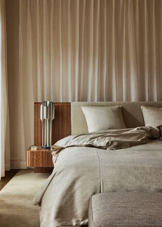 soft neutral bedroom with curtain behind bed, and built-in timber headboard with side tables and chrome table lamp