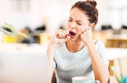 Tired female entrepreneur yawning in office. Horizontal shot.