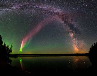 STEVE is visible as a pink band rising from the lower left to the upper right of the image, as seen with the Milky Way over Childs Lake in Manitoba, Canada. 