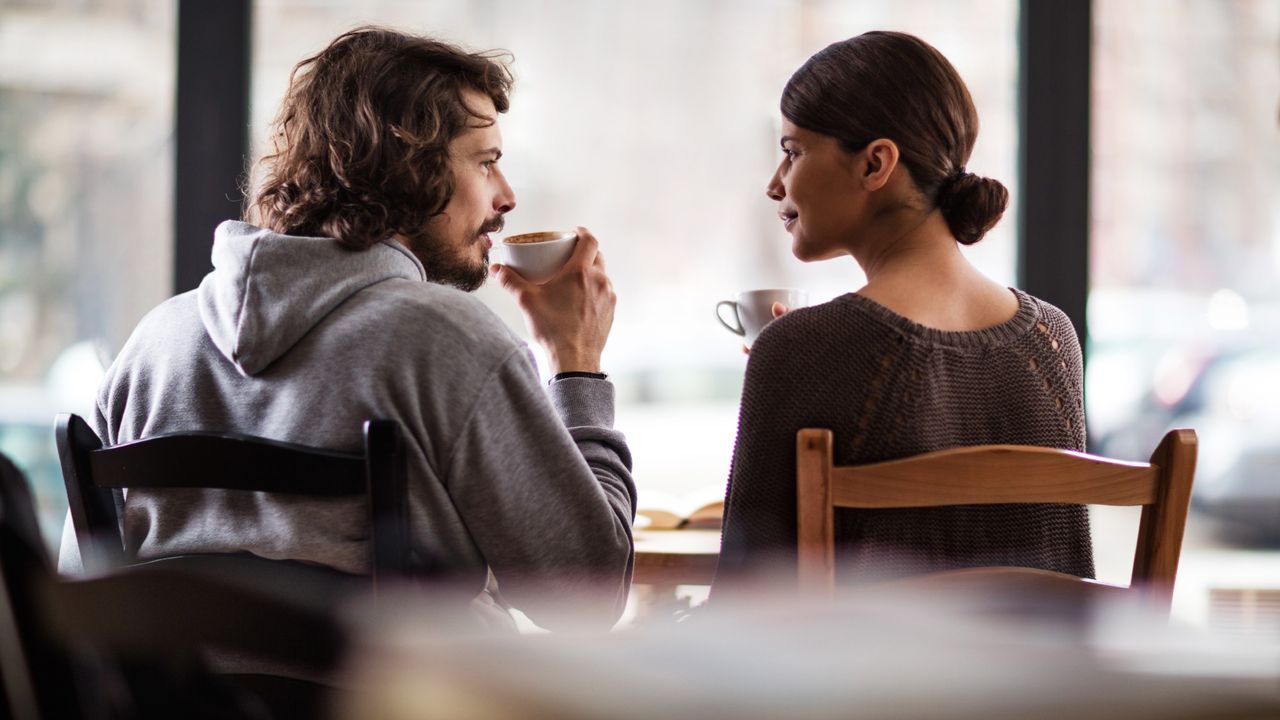 Rear view of young couple talking to each other while sitting in a cafe and drinking coffee.