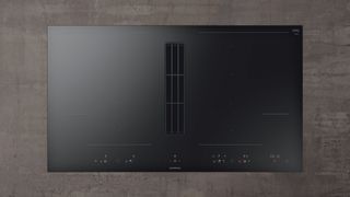 Black downdraft ventilator installed flush between the induction and gas hobs