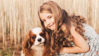 One of the best small dog breeds for kids, a Cavalier King Charles Spaniel and a young girl posing for a portrait