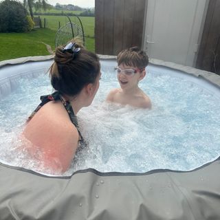 A mother and son sitting inside the filled Lay-Z-Spa Barabados inflatable hot tub . The boy has swimming googles on